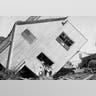 A house tipped on side with several boys standing in front after a flood in Galveston, Texas, 1900