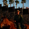 People in Mexico wave at U.S. Border Patrol agents on horseback patrolling the U.S.-Mexico border fence near San Diego, California.