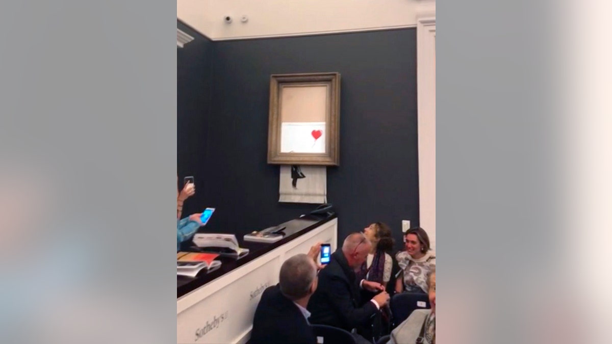 People watch as the spray-painted canvas "Girl with Balloon" by the artist Banksy self-destructs at Sotheby's, in London Oct. 5, 2018.