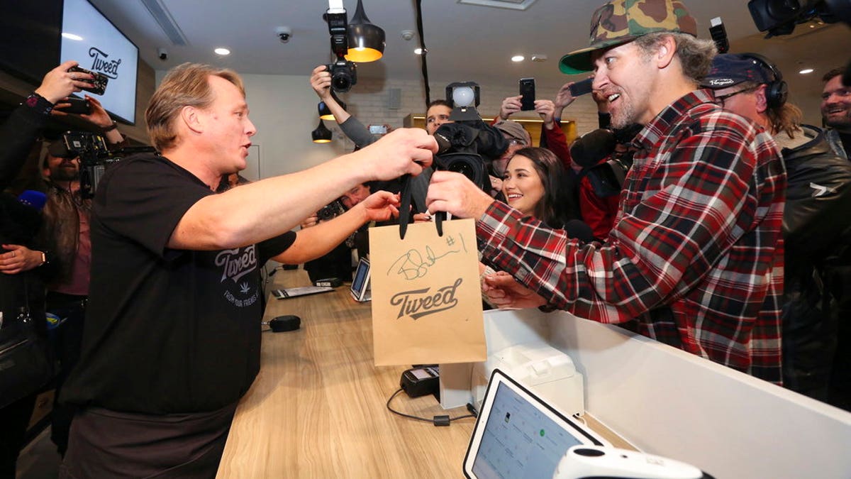 Canopy Growth CEO Bruce Linton, left to right, passes a bag with the first legal cannabis for recreation use sold in Canada to Nikki Rose and Ian Power at the Tweed shop on Water Street in St. John's N.L. at 12:01 am NDT on Wednesday Oct. 17, 2018