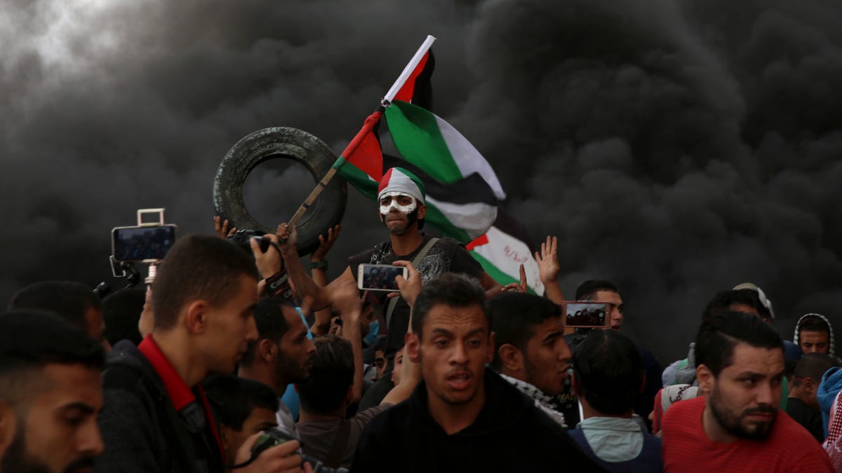 Protesters chant slogans while waves their national flags as others burn tires near the fence of the Gaza Strip border with Israel during a protest east of Gaza City, Friday, Oct. 26, 2018. (AP Photo/Adel Hana)
