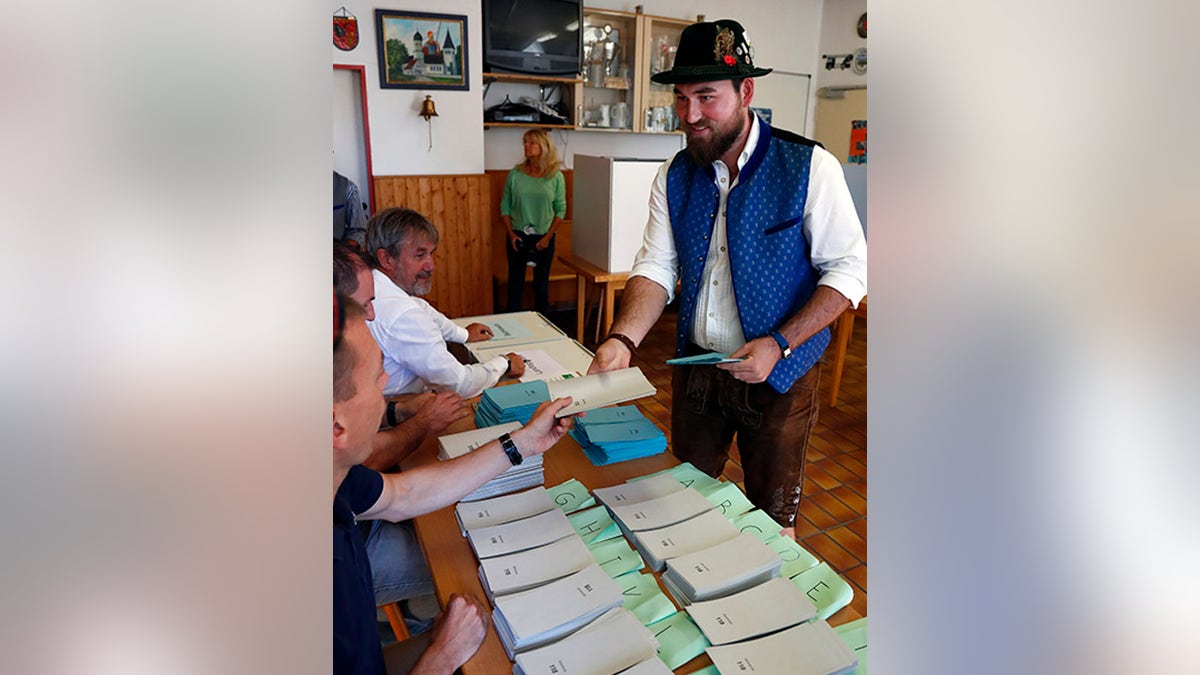 A young man in traditional Bavarian clothes gets the the ballot before casting his vote for the Bavarian state elections at a polling station in Maisach, Germany, Sunday, Oct. 14, 2018. (AP Photo/Matthias Schrader)