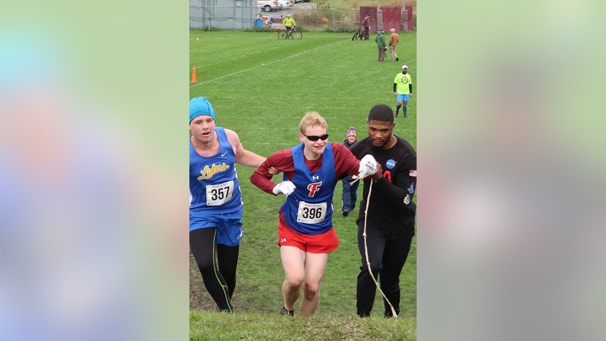 Cazenovia High School sophomore Jake Tobin, left, helps Fairport High School senior Luke Fortner, center, during a cross country race in Auburn, N.Y. Fortner, who is legally blind, fell towards the end of the race but was assisted by Tobin, and Jerry Thompson, right, his running aide.