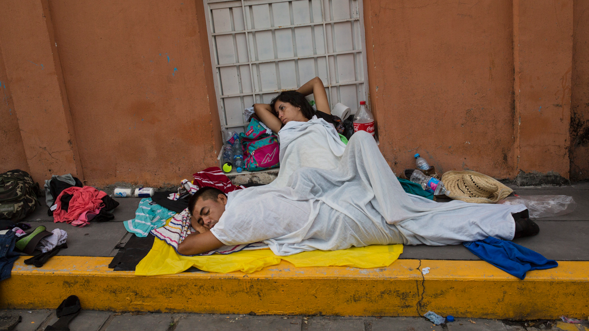 A migrant woman slowly begins to wake after sleeping on a sidewalk in Tapanatepec, Mexico, Sunday, Oct. 28, 2018. Thousands of migrants who are part of a caravan of Central Americans trying to reach the U.S. border took a break Sunday on their long journey toward the U.S. border.