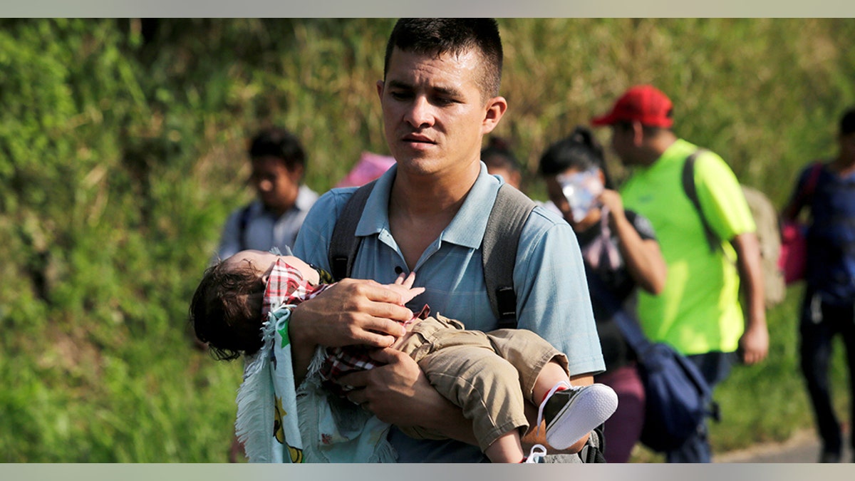 A young man carries a child in the Hondurans' caravan.