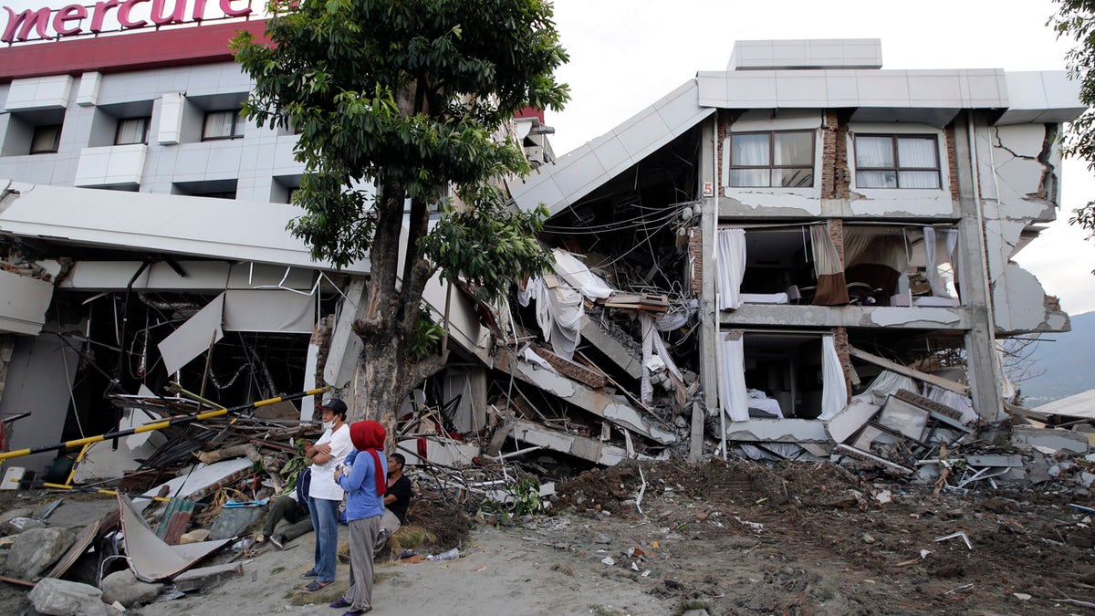 Filipinos stand beside the heavily damaged Mercure hotel after a massive earthquake and tsunami hit Palu, Central Sulawesi, Indonesia Thursday, Oct. 4, 2018. (AP Photo/Aaron Favila)