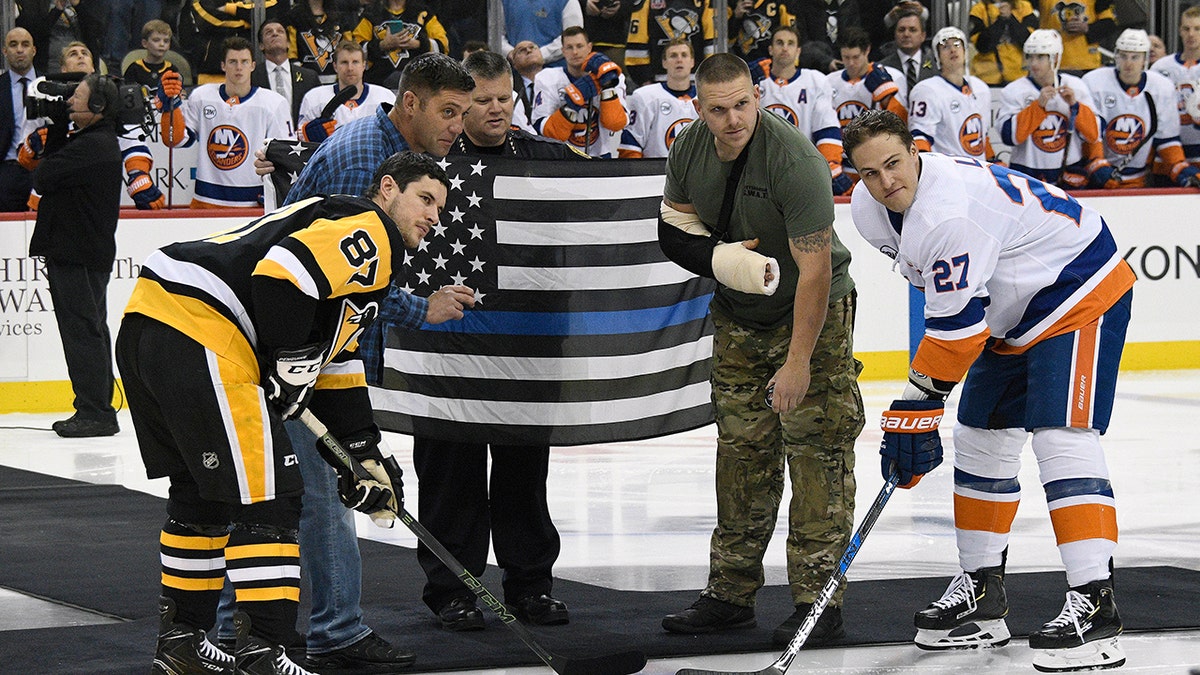Pittsburgh Police Officer Mike Smidga, Pittsburgh Police Chief Scott Schubert and Officer Anthony Burke take part in a ceremonial puck drop with Pittsburgh Penguins center Sidney Crosby (87) and New York Islanders left wing Anders Lee (27) before an NHL hockey game in Pittsburgh, Tuesday, Oct. 30, 2018.