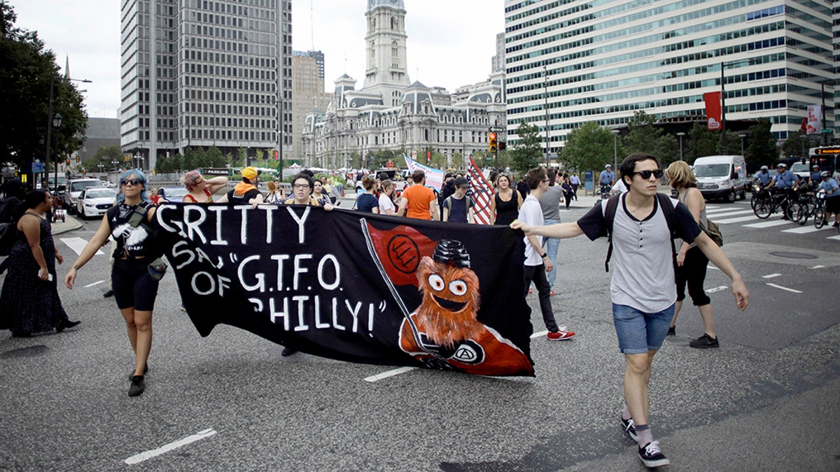 Demonstrators march through the Center City holding a banner with an image of the Philadelphia Flyers’ new mascot, Gritty, before a speech by President Trump at the National Electrical Contractors Convention on Tuesday. 