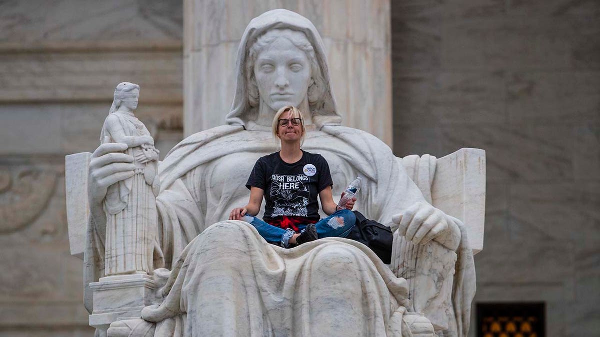 Jessica Campbell-Swanson, an activist from Denver, sits in the lap of a sculpture known as the Statue of Contemplation of Justice on the steps of the Supreme Court Building where she and others protested the confirmation of Brett Kavanaugh as the high court's newest justice, in Washington, Saturday, Oct. 6, 2018. (AP Photo/J. Scott Applewhite)
