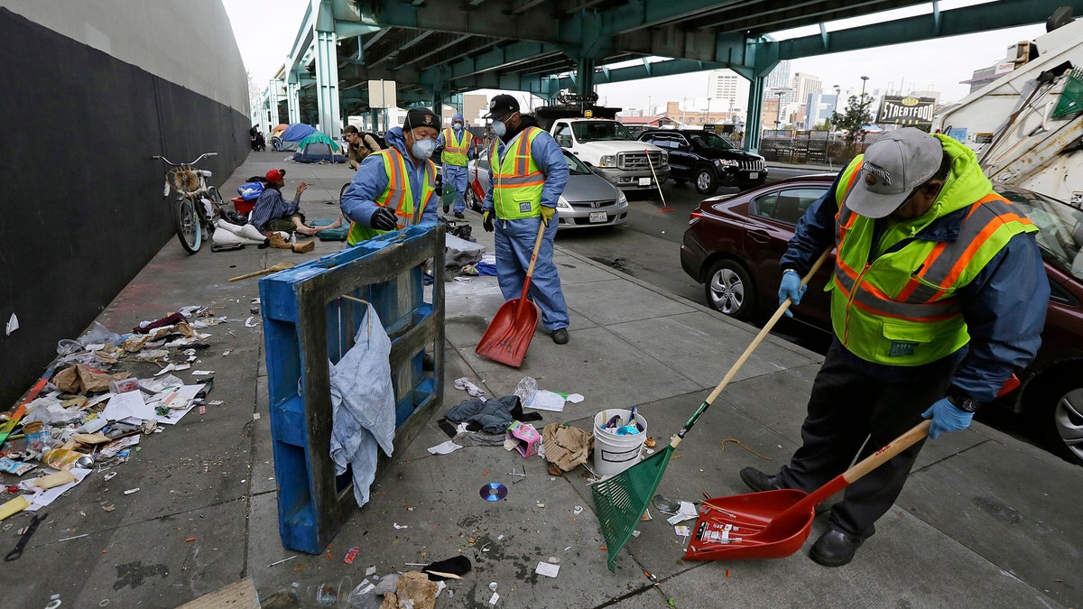 FILE - In this Feb. 26, 2016 file photo, city workers clear away debris that includes syringes from the remains of a tent city along Division Street in San Francisco. Sean Miller, a 24-year-old transplant, is offering a free app to make it easier for people to report waste - human and otherwise - and used needles and anything else gross on the famously dirty streets of San Francisco. (AP Photo/Eric Risberg, File)
