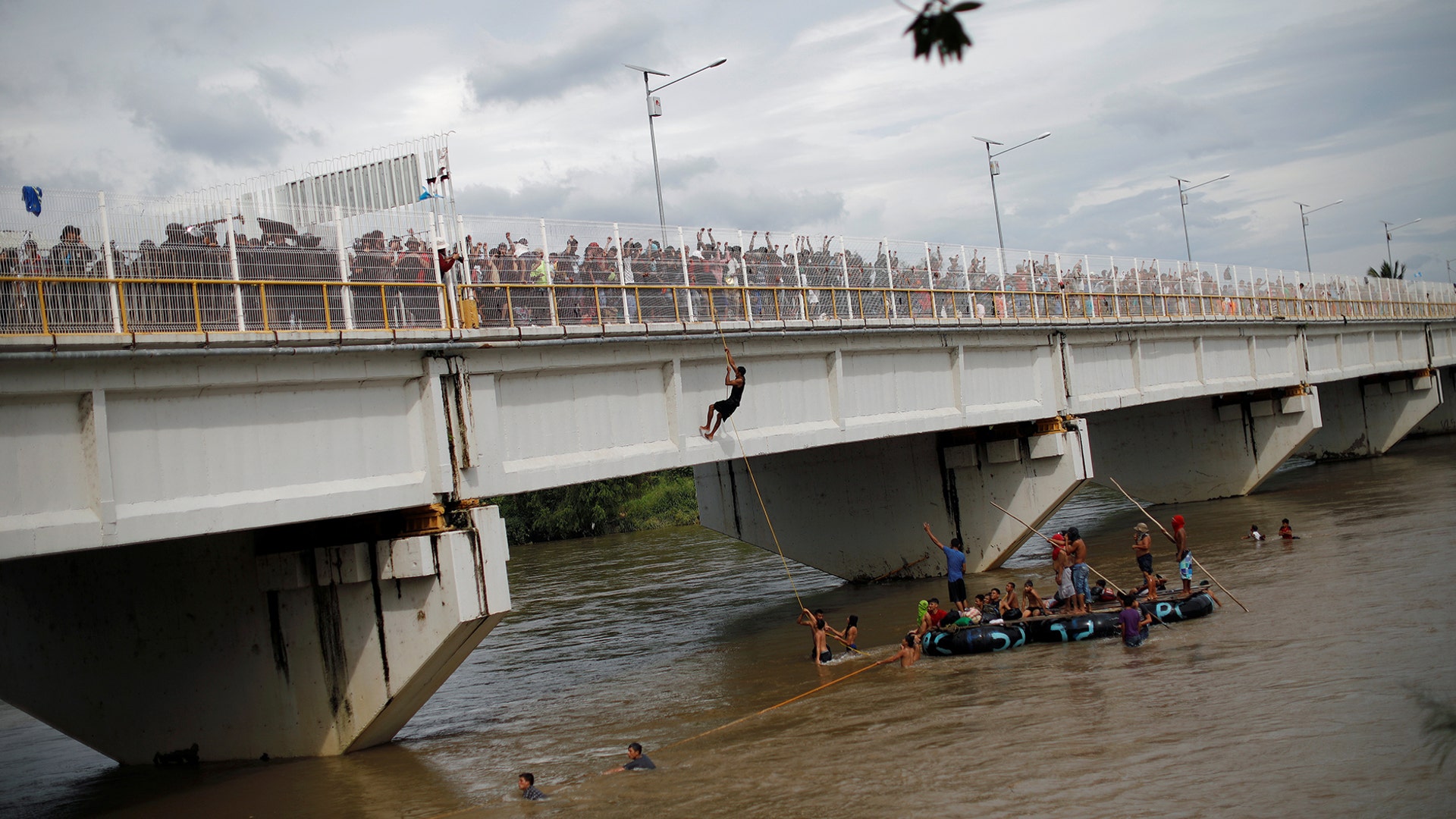 A Honduran migrant, part of a caravan trying to reach the United States, climbs from the bridge that connects Mexico and Guatemala with the help of fellow immigrants to avoid the border checkpoint in Ciudad Hidalgo, Mexico, on Oct. 19, 2018.