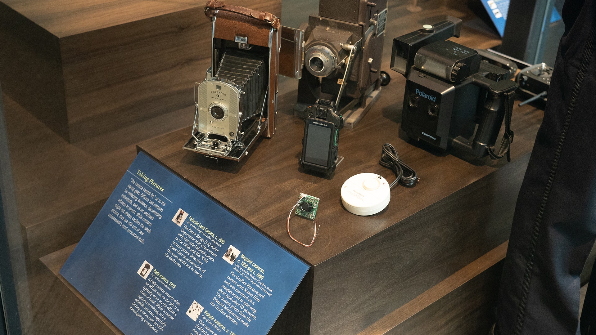 Historical models of photography and recording equipment, including body cameras, show the evolution of police surveillance.