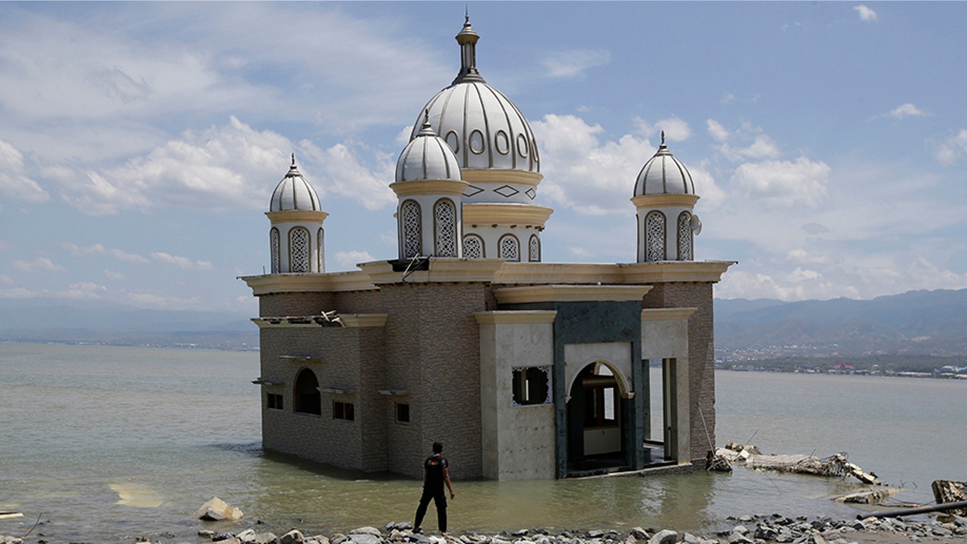 A man looks at a mosque that is isolated by water after its bridge was broken due to the massive earthquake and tsunami in Palu, Central Sulawesi, Indonesia Oct. 5, 2018.
