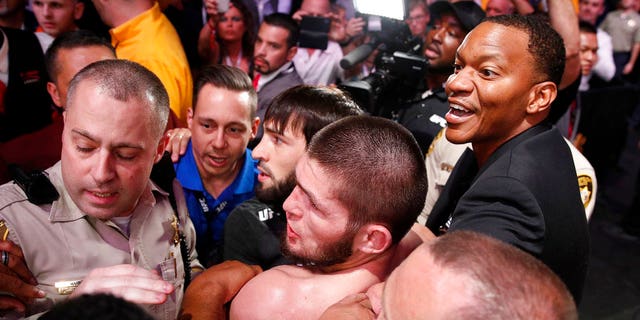 FILE: Khabib Nurmagomedov, bottom center, is held back outside of the cage after fighting Conor McGregor in a lightweight title mixed martial arts bout at UFC 229. 