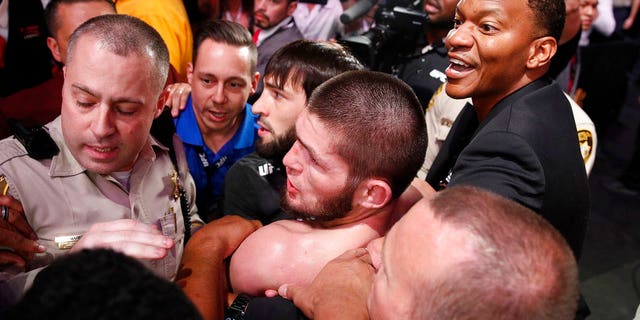 FILE: Khabib Nurmagomedov, bottom center, is held back outside of the cage after fighting Conor McGregor in a lightweight title mixed martial arts bout at UFC 229.