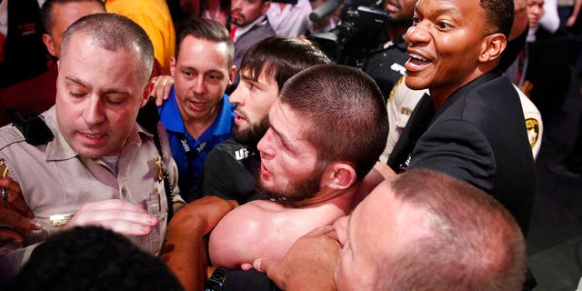 FILE: Khabib Nurmagomedov, bottom center, is held back outside of the cage after fighting Conor McGregor in a lightweight title mixed martial arts bout at UFC 229. 