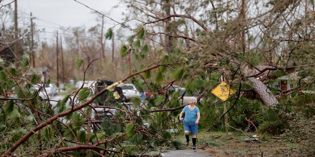 Carol Ralph walks through downed trees blocking her heavily damaged neighborhood just after Hurricane Michael passed through in Panama City.