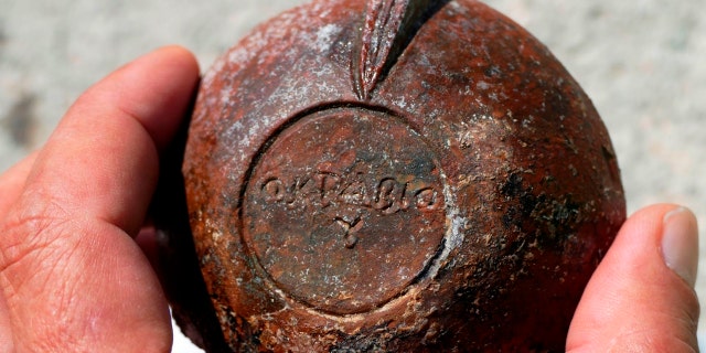 A man holds a 2nd-century A.D. terracotta lamp with the incised name of its maker, the Corinthian artisan Octavius, on the base, one of a group found on the seabed off the island of Fourni. 