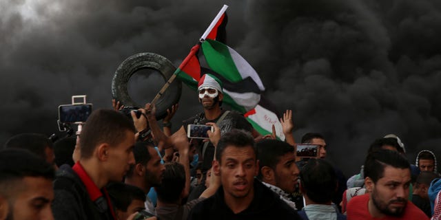 Protesters chant slogans while waves their national flags as others burn tires near the fence of the Gaza Strip border with Israel during a protest east of Gaza City, Friday, Oct. 26, 2018. (AP Photo/Adel Hana)