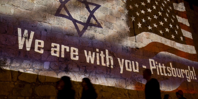 People walk past a projection on the Old City wall in Jerusalem, Sunday, Oct. 28, 2018 in a commemoration of the victims of a deadly shooting at a Pittsburgh synagogue. A shooter opened fire at a Pittsburgh synagogue, killing 11 people in one of the deadliest attacks on Jews in U.S. history. (AP Photo/Dusan Vranic)
