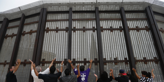 FILE - In this July 14, 2013, file photo, pastors and others raise their arms on the San Diego side of a border fence during a cross-border Sunday religious service with others on the Tijuana, Mexico side of the fence. The Tijuana and San Diego border crossing is the world's busiest land border crossing, but also now sees relatively few illegal crossings. (AP Photo/ Gregory Bull, File)