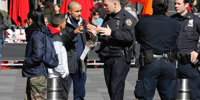 A New York City Police Department officer assists a person in New York's Times Square, Friday, Oct. 19, 2018. New reforms aimed at improving police interactions in New York City include requirements that officers hand out their business cards to people they stop and explain why law enforcement activity is taking place. (AP Photo/Richard Drew)