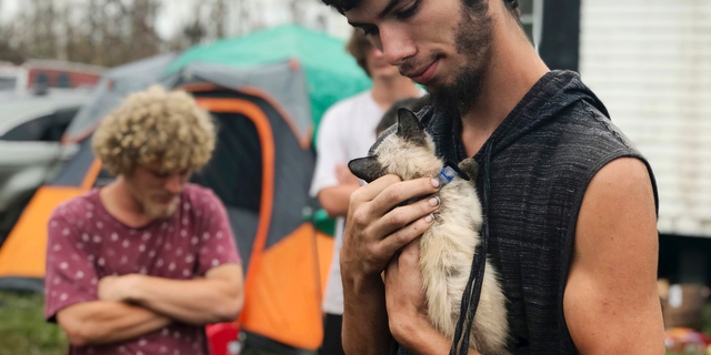 In this Oct. 23, 2018 photo, Ronald Lauricella cradles a kitten in his front yard in Bay County, Fla.,. The rural Bay County resident says some on the outskirts of the cities aren't getting needed services like electricity as fast as the populated areas. (AP Photo/Tamara Lush)