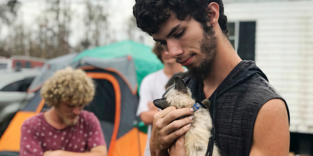 In this Oct. 23, 2018 photo, Ronald Lauricella cradles a kitten in his front yard in Bay County, Fla.,. The rural Bay County resident says some on the outskirts of the cities aren't getting needed services like electricity as fast as the populated areas. (AP Photo/Tamara Lush)