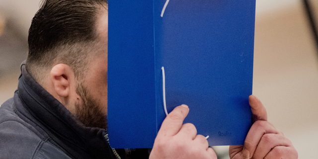 Niels Hoegel covers his face with a folder as he arrives at the Oldenburg district court at the Weser Ems halls in Oldenburg, Germany, Tuesday, Oct. 30