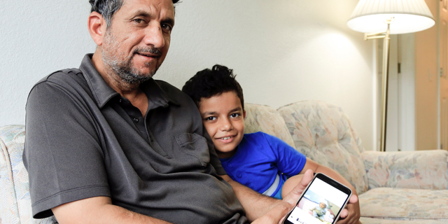 In this Sept. 29, 2018 photo, Hadi Mohammed sits with his 9 year old son Mohammed Ghaleb, as he displays a photo of his son as a baby in Baghdad, in their Lincoln, Neb. apartment. Death threats drove Hadi Mohammed out of Iraq and to a small apartment in Nebraska, where he and his two young sons managed to settle as refugees. But the danger hasn’t been enough to allow his wife to join them. (AP Photo/Nati Harnik)
