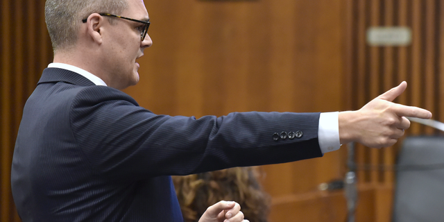 Assistant prosecutor Matthew Penney acts like he's pulling the trigger of a taser as he faces the jury during his opening statement Tuesday, Oct, 23, 2018, in Detroit, Mich., during the trial of former Michigan state trooper Mark Bessner. A prosecutor has told jurors that a Michigan state trooper used unreasonable force when he fired a Taser at a Detroit teenager who then crashed an all-terrain vehicle and died. Trial opened Tuesday for Bessner, who is charged with second-degree murder in the death of 15-year-old Damon Grimes. (Todd McInturf /Detroit News via AP)