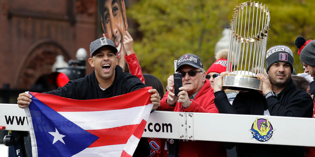 Boston Red Sox manager Alex Cora, left, waves the flag of Puerto Rico as coach Ramon Vazquez holds the championship trophy during a parade to celebrate the team's World Series championship over the Los Angeles Dodgers, Wednesday, Oct. 31, 2018, in Boston. (AP Photo/Elise Amendola)