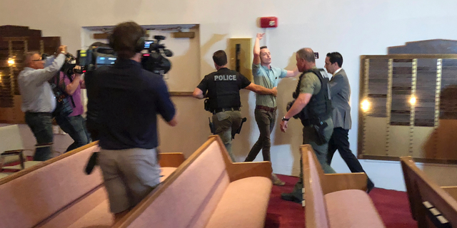 Police officers escort protester Jacob Engels from a Florida synagogue Thursday, Oct. 25, 2018, in Plantation, Fla., before a speech by Democratic gubernatorial candidate Andrew Gillum. Engel shouted Gillum is "a radical Jew hater who supports mob violence" as he was removed by Plantation, Florida, police officers. Gillum later told the crowd that support for Israel should be bipartisan and that accusations he is an anti-Semite are false. (AP Photo/Terry Spencer)