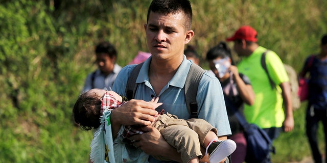 A young man carries a child in the Hondurans' caravan.