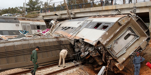 A police officer and train workers standing by a derailed train Tuesday near Sidi Bouknadel, Morocco.