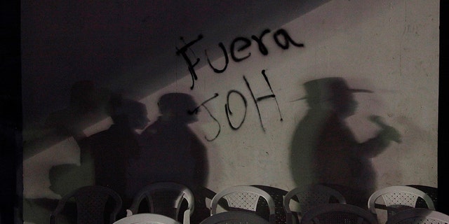 FILE - In this Feb. 3, 2018 file photo, the shadow of ousted Honduran President Manuel Zelaya is cast on a wall covered by the message "Get out JOH," referring to President Juan Orlando Hernandez, in Central Park, Tegucigalpa, Honduras. Since then-President Manuel Zelaya was ousted in a coup in 2009, the country’s political situation has been tense. The polarization increased after the November 2017 election in which current President Juan Orlando Hernandez was re-elected in a result marred by electoral irregularities, and denounced by his opponent as outright fraud. Extensive protests over the election were repressed with “indiscriminate and excessive use of force,” according to the Inter-American Commission on Human Rights. (AP Photo/Fernando Antonio, File)