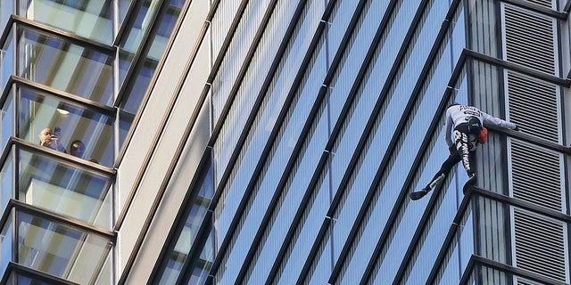 People watch from inside the building as urban climber dubbed the French Spider-Man, Alain Robert scales the outside of Heron Tower building in London