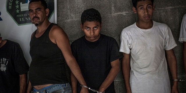 Suspected members of the 18th Street gang stand handcuffed in pairs at a police station in Panchimalco, near San Salvador, El Salvador. The gangs trace their origins to street life in cities such as Los Angeles, where many Salvadorans sought refuge during their country’s 1980-1992 civil war. (AP Photo/Manu Brabo, File)