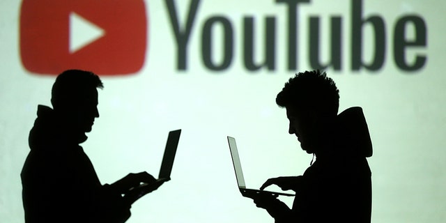 Silhouettes of mobile device users are seen next to a screen projection of Youtube logo in this picture illustration taken March 28, 2018. REUTERS/Dado Ruvic/Illustration - RC1502FFC0B0