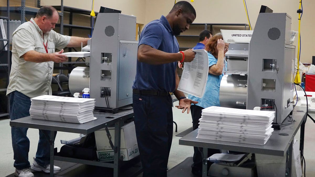 Election workers place ballots into electronic counting machines, Sunday, Nov. 11, 2018, at the Broward Supervisor of Elections office in Lauderhill, Fla. The Florida recount began Sunday morning in Broward County. (Joe Cavaretta /South Florida Sun-Sentinel via AP)