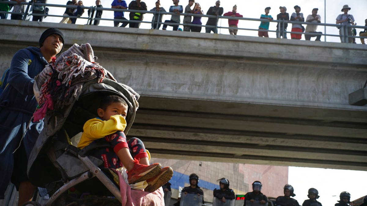 A migrant man pushes a child in a baby stroller past a cordon of riot police as he joins a small group of migrants trying to cross the border together at the Chaparral border crossing in Tijuana, Mexico, Thursday, Nov. 22, 2018. A small group of Central American migrants marched peacefully to a border crossing in Tijuana Thursday to demand better conditions and push to enter the U.S. (AP Photo/Ramon Espinosa)