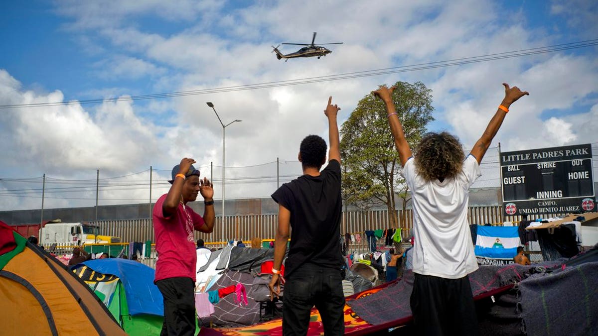 Migrants wave at U.S. border control helicopters flying near the Benito Juarez Sports Center serving as a temporary shelter for Central American migrants, in Tijuana, Mexico, Saturday, Nov. 24, 2018. The mayor of Tijuana has declared a humanitarian crisis in his border city and says that he has asked the United Nations for aid to deal with the approximately 5,000 Central American migrants who have arrived in the city. (AP Photo/Ramon Espinosa)