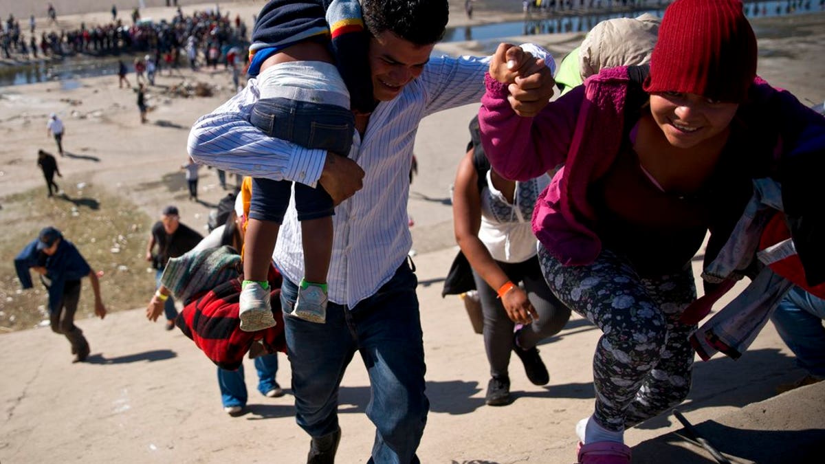 Migrants walk up a riverbank at the Mexico-U.S. border after getting past a line of Mexican police at the Chaparral border crossing in Tijuana, Mexico, Sunday, Nov. 25, 2018, as they try to reach the U.S. The mayor of Tijuana has declared a humanitarian crisis in his border city and says that he has asked the United Nations for aid to deal with the approximately 5,000 Central American migrants who have arrived in the city. (AP Photo/Ramon Espinosa)