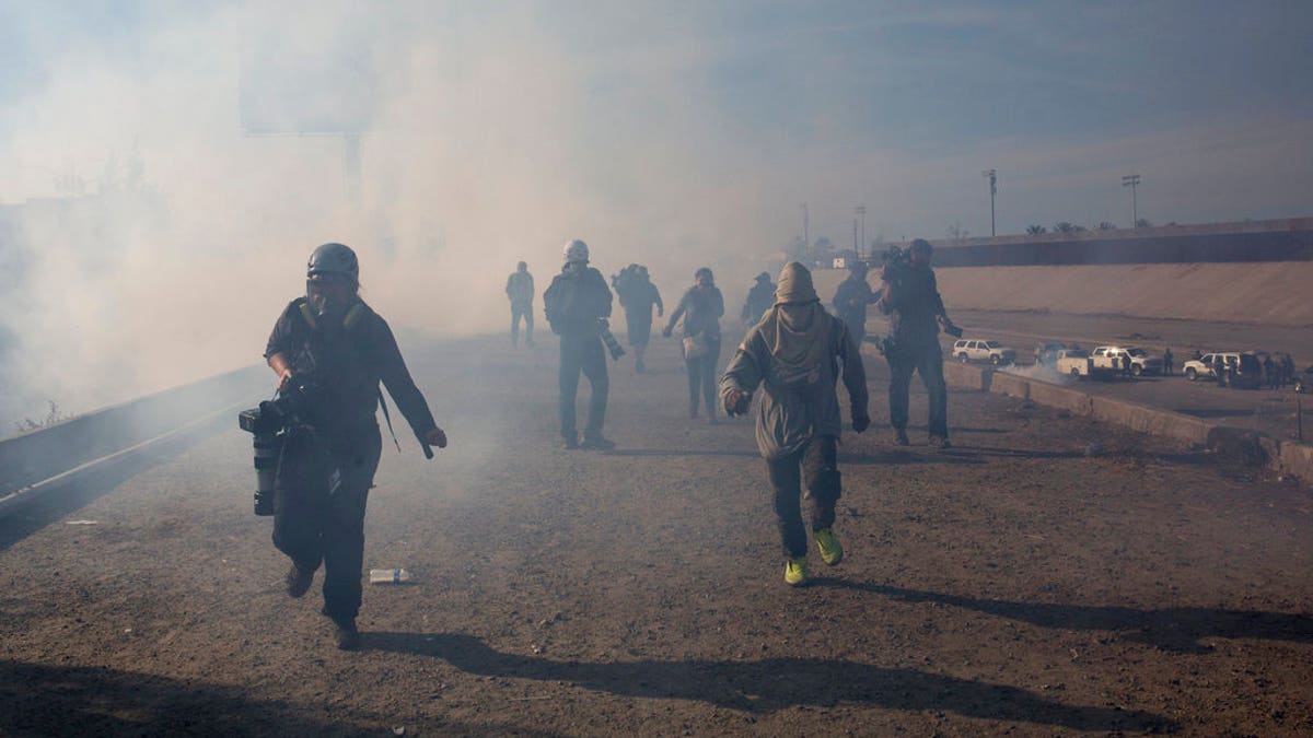 Migrants run from tear gas launched by U.S. agents, amid photojournalists covering the Mexico-U.S. border, after a group of migrants got past Mexican police at the Chaparral crossing in Tijuana, Mexico, Sunday, Nov. 25.