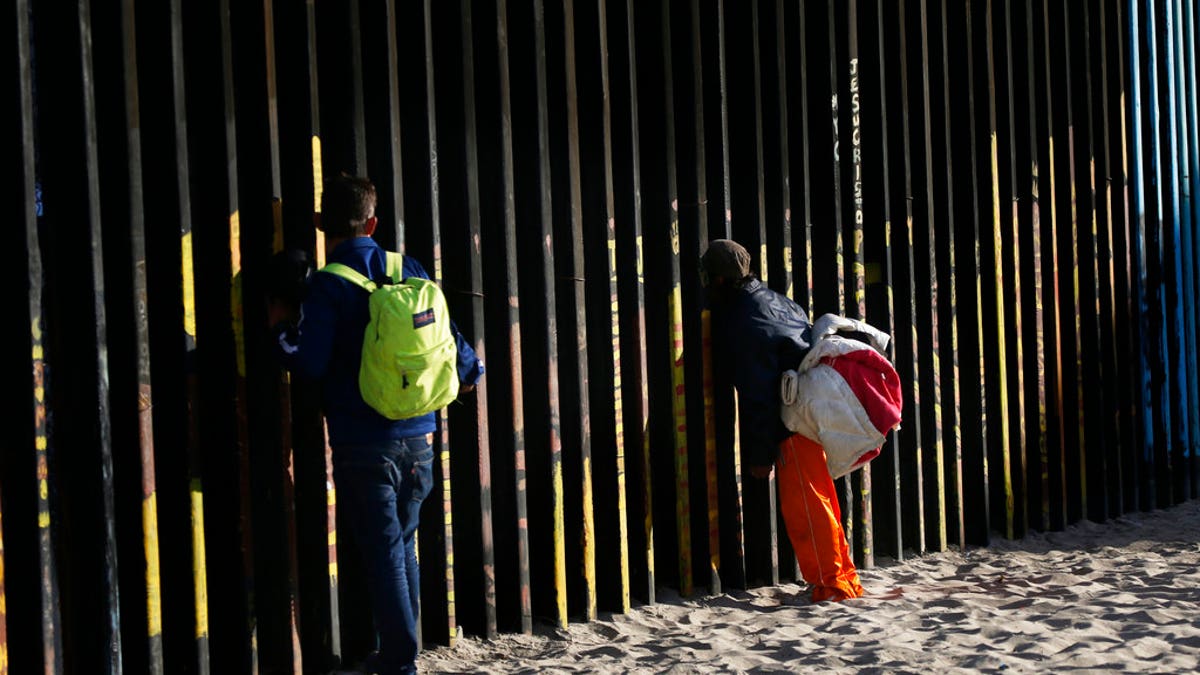 Central American migrants look through the border structure expecting top make an illegal crossing into the U.S., seen from the Mexican side where the border meets the Pacific Ocean, Friday, Nov. 16, 2018. As thousands of migrants of asylum-seekers converge on the doorstep of the United States, what they won't find are armed American soldiers standing guard, that's because U.S. military troops are prohibited from carrying out law enforcement duties. (AP Photo/Marco Ugarte)
