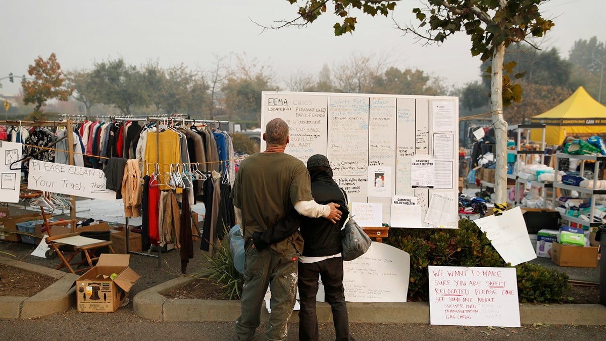 Tera Hickerson, right, and Columbus Holt embrace as they look at a board with information for services at a makeshift encampment outside a Walmart store for people displaced by the Camp Fire.