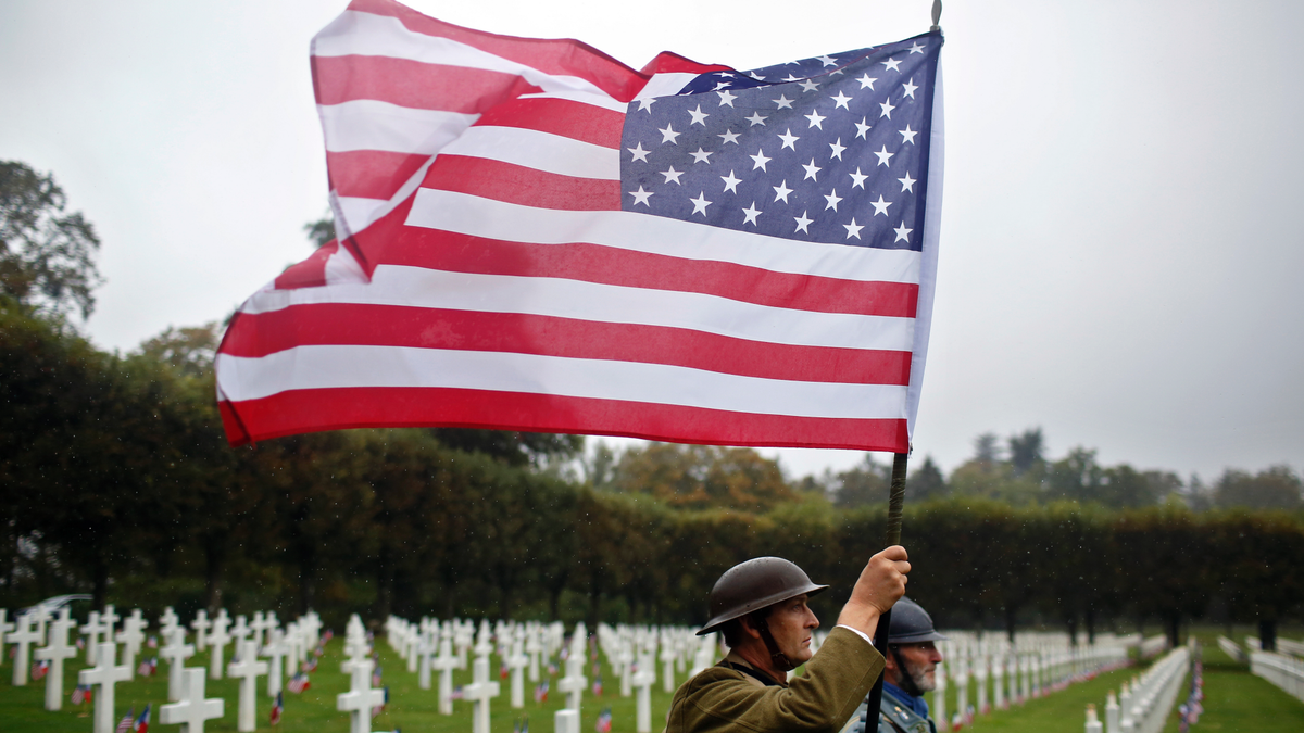 FILE In this Sunday, Sept. 23, 2018 file photo, re-enactors in World War I military uniforms carry an American flag in the Meuse-Argonne Cemetery, northeastern France. After the United States declared war on Germany in April 1917, its standing army of 127,500 became an armed force of 2 million within 1 ½ years. On Nov 11, 1918, allies like Britain and France were exhausted, Germany was as good as defeated and U.S. Gen. John J. Pershing had another 2 million troops ready to come over. (AP Photo/Thibault Camus, File)