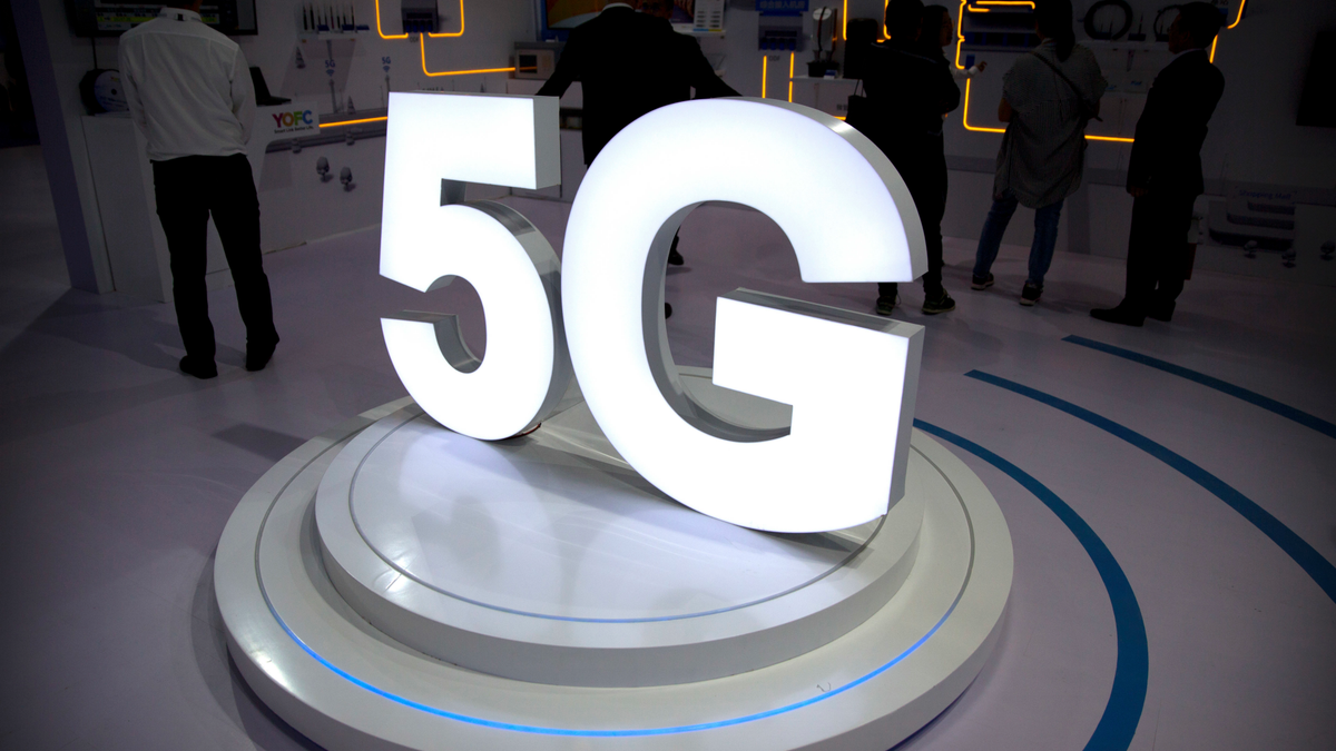 FILE- In this Sept. 26, 2018, file photo visitors stand near a 5G logo at a display the PT Expo in Beijing. Telecommunications equipment maker CommScope Holding Co. is paying about $5.7 billion for Arris International Plc. as it prepares for the entrance of faster 5G service to the wireless market. (AP Photo/Mark Schiefelbein, File)