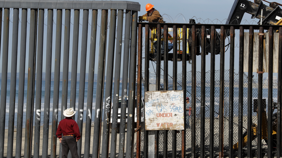 A man on the U.S. side of the border, top, works on the border structure as a man standing on the beach looks on, seen from Tijuana, Mexico, Thursday, Nov. 15, 2018. Members of a migrant caravan from Central America continued to arrive by the hundreds in the Mexican border city of Tijuana. (AP Photo/Gregory Bull)