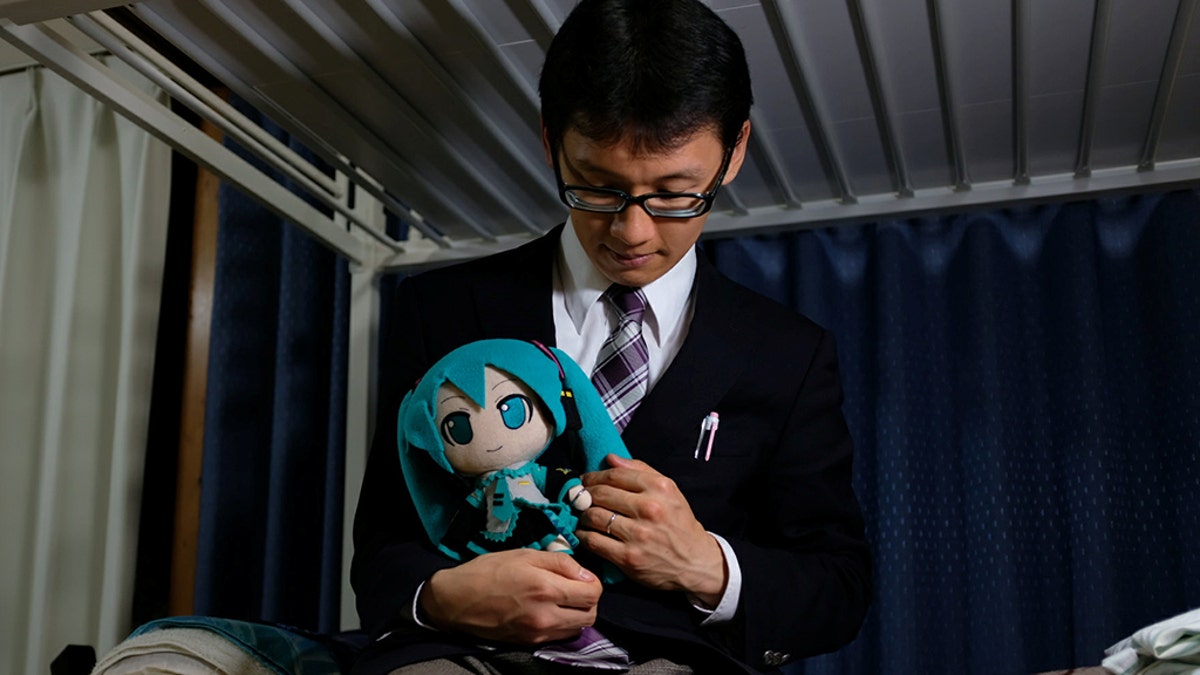 Akihiko Kondo, 35, poses for a photograph with a doll modeled after virtual reality singer Hatsune Miku, wearing their wedding rings, at his apartment after marrying her in Tokyo, Japan.